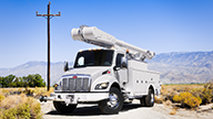 Peterbilt Model 537 Medium Duty White Truck with White Bucket Boom and Utility Box on Desolate Road and Mountainous Background - Thumbnail